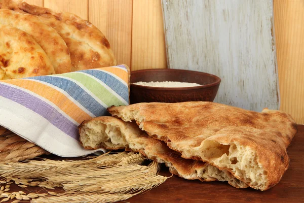 Pita breads in basket with spikes and flour on table on wooden background — Stock Photo, Image