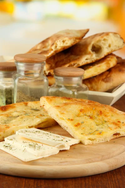 Pita breads with cheese on wooden stand and spice on table on bright background — Stock Photo, Image