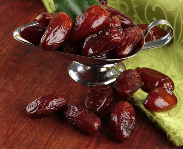 Dried dates in metal dish with napkin on wooden background — Stock Photo, Image