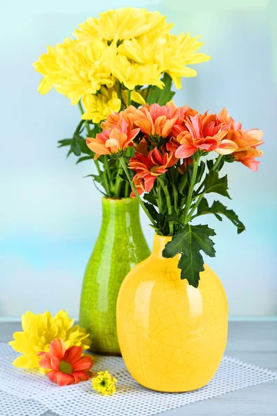 Beautiful flowers in vases, on wooden table, on light background — Stock Photo, Image