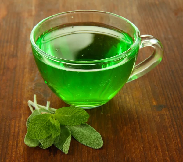 Tazza trasparente di tè verde con salvia su sfondo di legno — Foto Stock