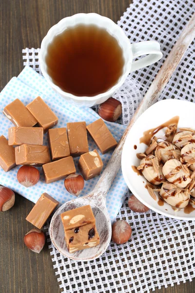 Many toffee in spoon and cup of tea on napkins on wooden table — Stock Photo, Image