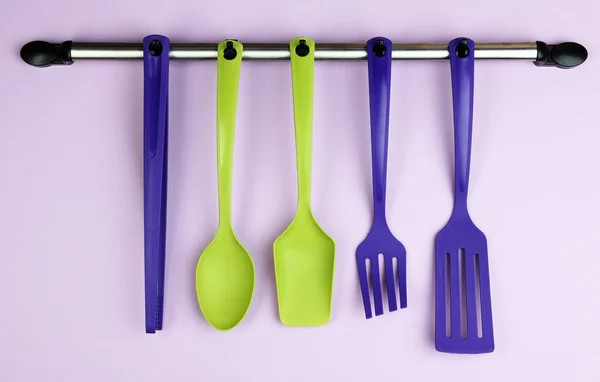 Plastic kitchen utensils on silver hooks on lilac background — Stock Photo, Image