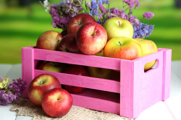 Saftiga äpplen i rutan på vita träbord på naturliga bakgrund — Stockfoto