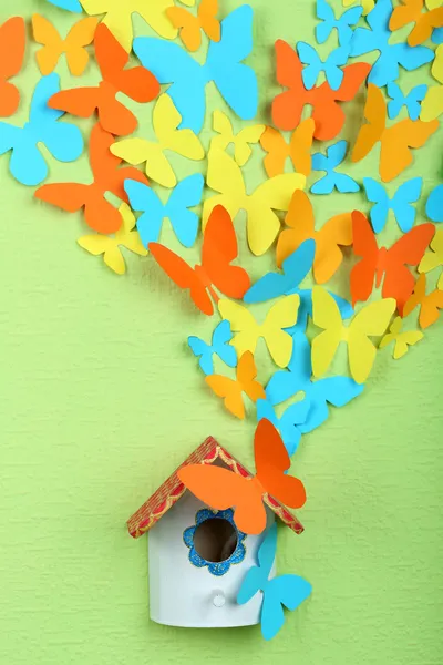 Paper butterflies fly out of nesting box on green wall background — Stock Photo, Image