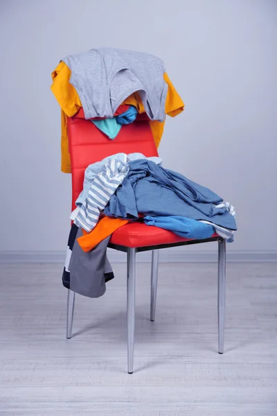 Heap of clothes on color chair, on gray background — Stock Photo, Image