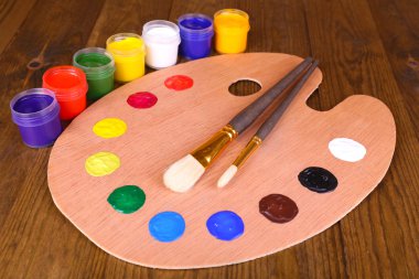 Wooden art palette with paint and brushes on table close-up clipart