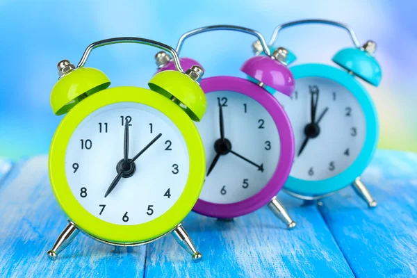Relojes de alarma de colores en la mesa sobre fondo azul —  Fotos de Stock