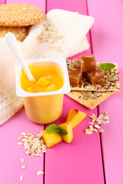 Läckra yoghurt med bitar av färsk frukt, kakor och flingor, på färg trä bakgrund — Stock fotografie