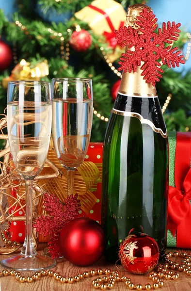 Láhev šampaňského s brýlemi a vánoční koule na dřevěný stůl na vánoční stromeček pozadí — Stock fotografie