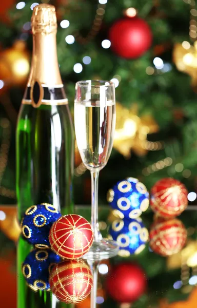 Bottle of champagne with glass and Christmas balls on Christmas tree background — Stock Photo, Image