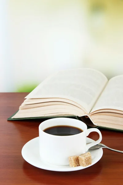Xícara de café com açúcar e livro sobre mesa de madeira fundo brilhante — Fotografia de Stock