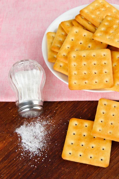 Deliziosi cracker con sale e tovagliolo su sfondo di legno — Foto Stock