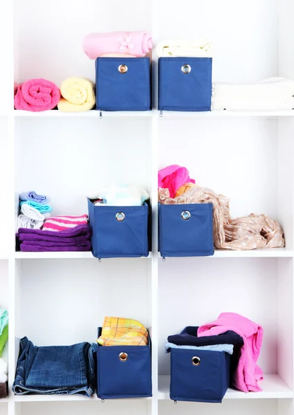 Blue textile boxes with towels and clothes in white shelves — Stock Photo, Image