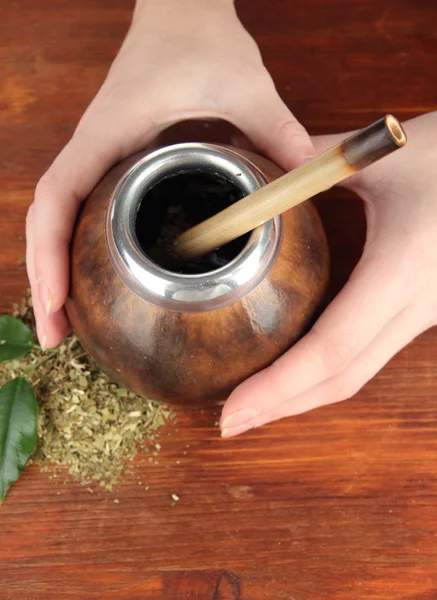 Manos de mujer sosteniendo calabaza y bombilla con yerba mate sobre fondo de madera —  Fotos de Stock