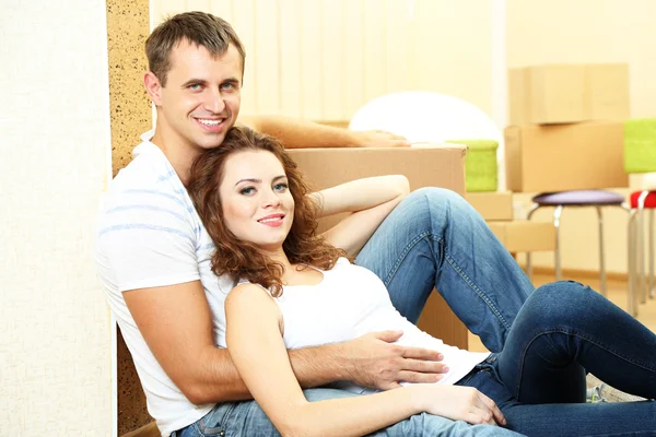 Young couple with boxes in new home on room background — Stock Photo, Image