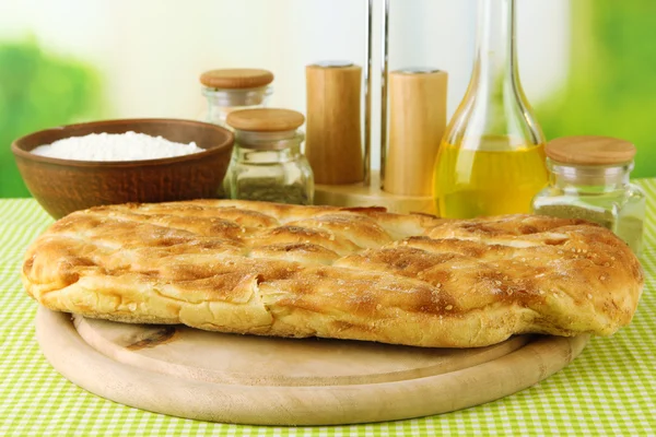 Pita bread on wooden stand with spices on tablecloth on bright background — Stock Photo, Image