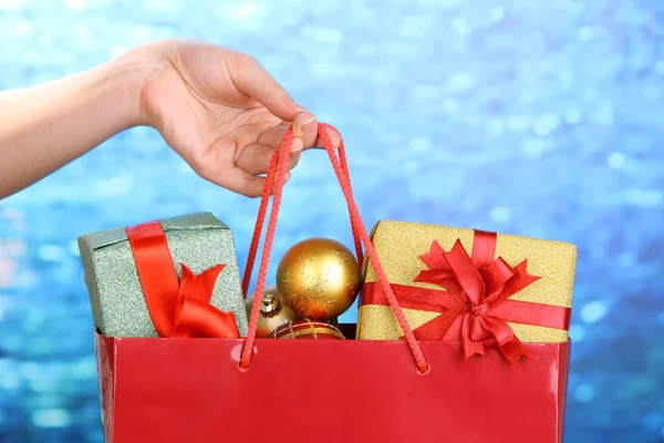 La mano sostiene el paquete con bolas de Año Nuevo y regalos sobre fondo azul —  Fotos de Stock