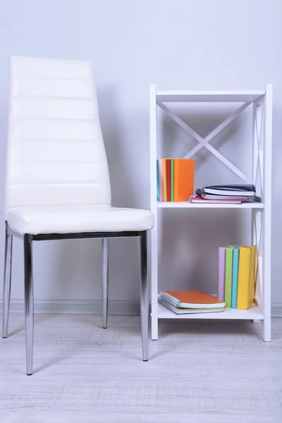 Beautiful interior with modern color chair, books on wooden stand, on wall background — Stock Photo, Image