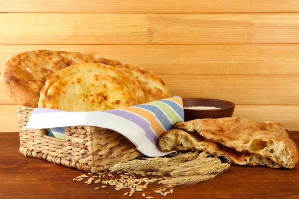 Pita breads in basket with spikes and flour on table on wooden background — Stock Photo, Image