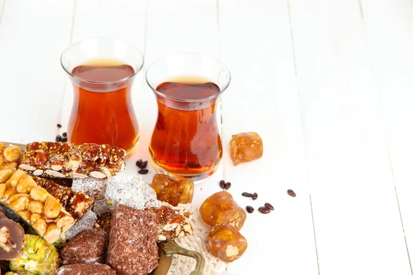 Tasty oriental sweets on tray and glasses of tea, on white wooden background — Stock Photo, Image