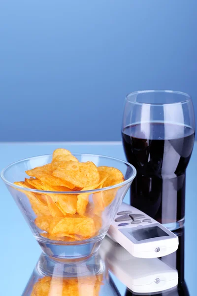 Chips in bowl, cola and TV remote on blue background — Stock Photo, Image