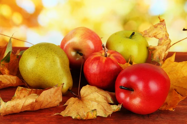 Hermosas manzanas maduras y pera con hojas amarillas sobre la mesa sobre fondo brillante —  Fotos de Stock