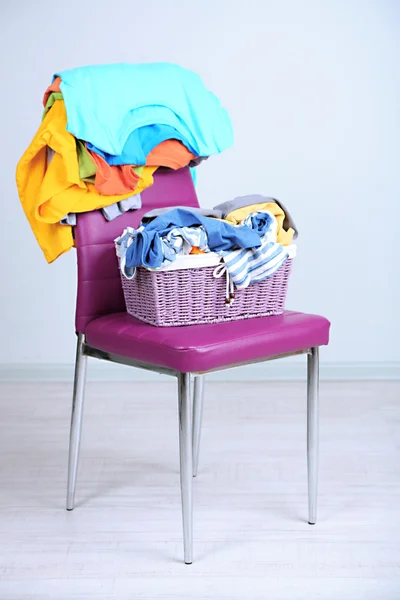 Kleiderhaufen auf farbigem Stuhl, auf grauem Hintergrund — Stockfoto