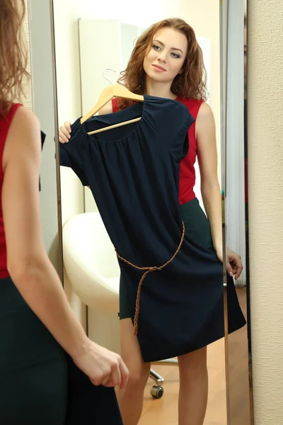Hermosa chica tratando de vestir cerca del espejo en la habitación — Foto de Stock