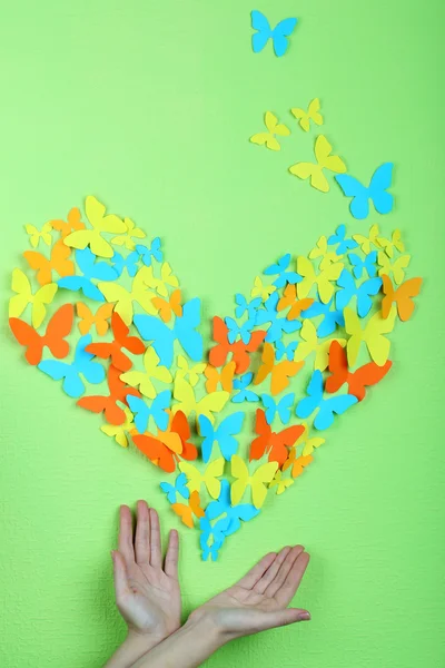 Paper butterflies on hands on green wall background — Stock Photo, Image