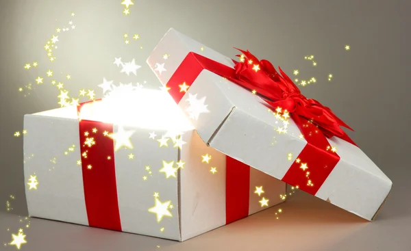 Gift box with bright light on it on grey background — Stock Photo, Image