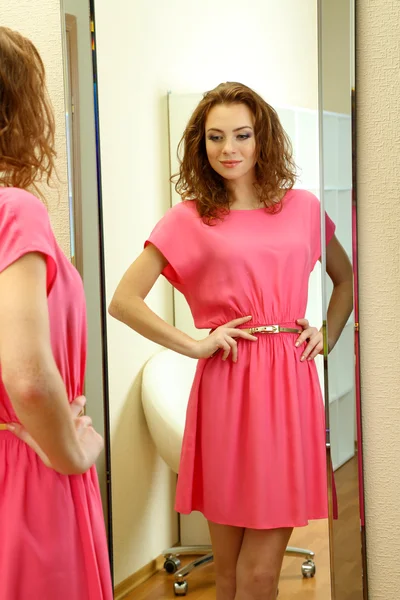 Beautiful girl trying dress near mirror in room — Stock Photo, Image