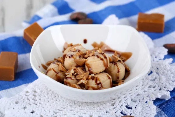 Many toffee in bowl on napkin on wooden table — Stock Photo, Image