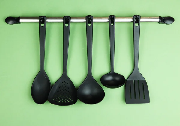 Plastic kitchen utensils on silver hooks on green background — Stock Photo, Image