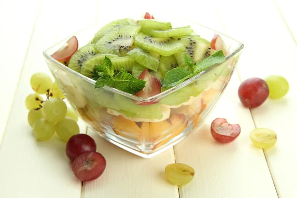 Sałatka smaczny owoc w szklanej misce, na biały drewniany stół — Zdjęcie stockowe