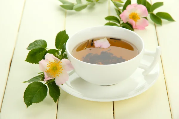 Tasse Kräutertee mit hippen Rosenblüten auf weißem Holztisch — Stockfoto