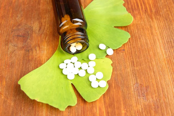 Листья гинкго билоба и бутылка с лекарствами на деревянном фоне — стоковое фото