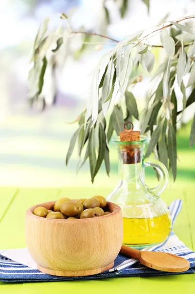 Olive oil and olives in bowl on napkin on wooden table on nature background — Stock Photo, Image