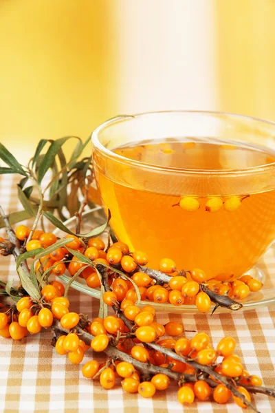 Branches of sea buckthorn with tea on tablecloth on bright background — Stock Photo, Image