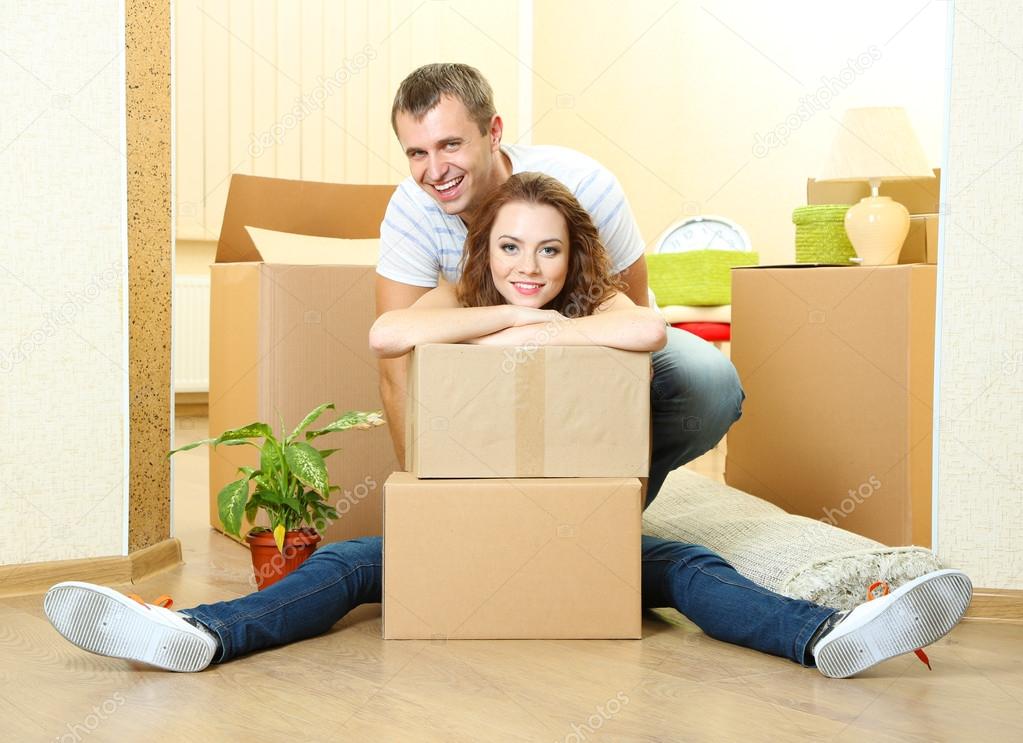 Young couple with boxes in new home on room background