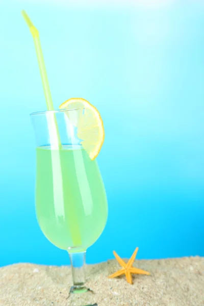 Beach cocktail in sand on blue background — Stock Photo, Image