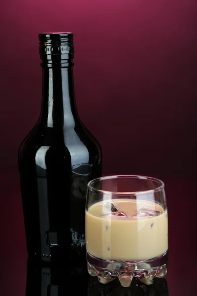 Baileys liqueur in bottle and glass on pink background — Stock Photo, Image