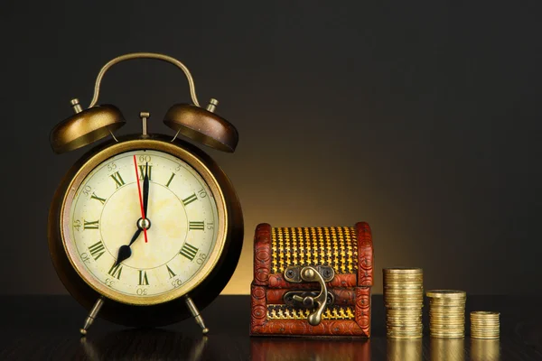 Orologio antico e monete su tavolo di legno su sfondo di colore scuro — Foto Stock