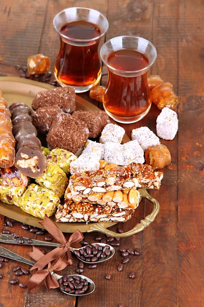 Smakelijke oosterse snoepjes op lade en glazen thee, op grijze houten achtergrond — Stockfoto