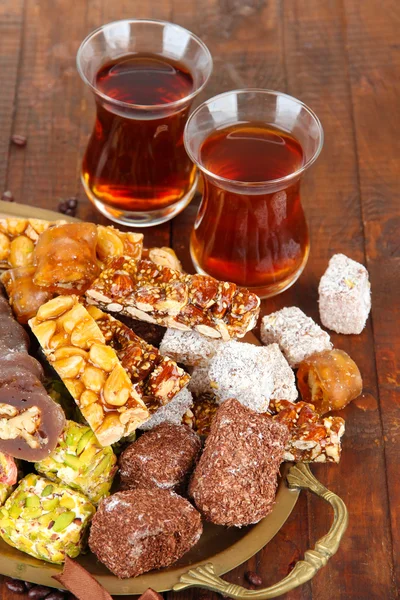 Tasty oriental sweets on tray and glasses of tea, on grey wooden background — Stock Photo, Image