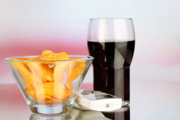 Chips in bowl, cola and TV remote on bright background — Stock Photo, Image