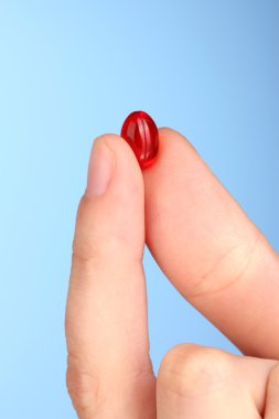 Kırmızı hapı mavi arka plan yakın çekim tutan kadının el