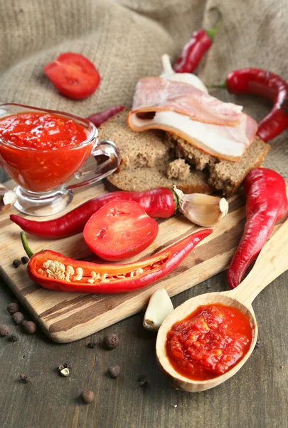 Composition with salsa sauce on bread,, red hot chili peppers and garlic, on sackcloth, on wooden background — Stock Photo, Image