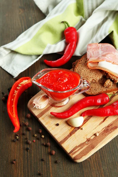Composición con salsa sobre pan, ají rojo picante y ajo, sobre servilleta, sobre fondo de madera — Foto de Stock
