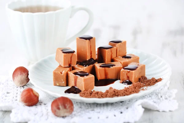 Many toffee on plate and cup of tea on napkin on wooden table — Stock Photo, Image